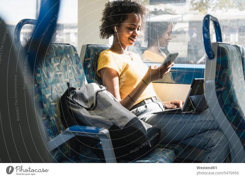 Young woman with earphones using smartphone and tablet on a train human human being human beings humans person persons adult grown-up grown-ups grownup grownups