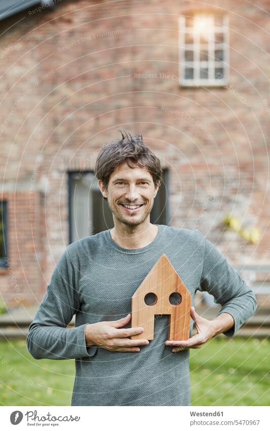 Portrait of smiling man in front of his home holding house model men males portrait portraits smile models houses Adults grown-ups grownups adult people persons