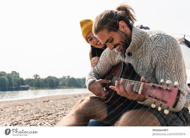 Happy young couple with guitar at the riverside guitars riverbank twosomes partnership couples happiness happy stringed instrument stringed instruments
