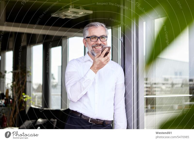 Smiling businessman standing at French door using cell phone on the phone call telephoning On The Telephone calling French Door Businessman Business man
