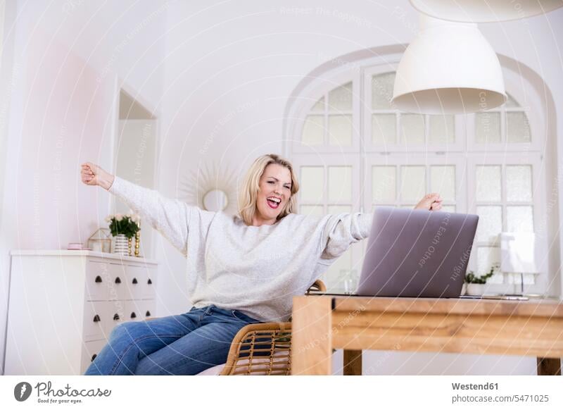 Portrait of happy blond mature woman with laptop at home females women blond hair blonde hair happiness portrait portraits Laptop Computers laptops notebook