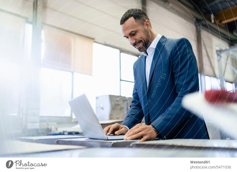 Smiling businessman using laptop in a factory human human being human beings humans person persons Mixed Race mixed race ethnicity mixed-race Person 1