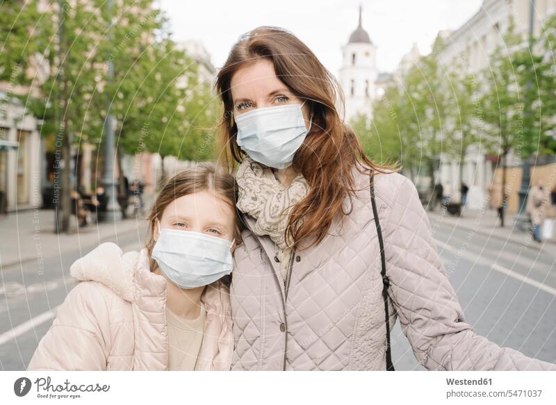 Mother and daughter wearing masks standing on street in city color image colour image outdoors location shots outdoor shot outdoor shots day daylight shot