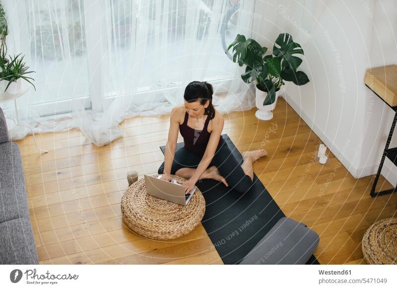 Woman sitting on gym mat at home using laptop Curtains Draperies Drapery windows Technological technologies The Internet e-mailing e-mails electronic mail