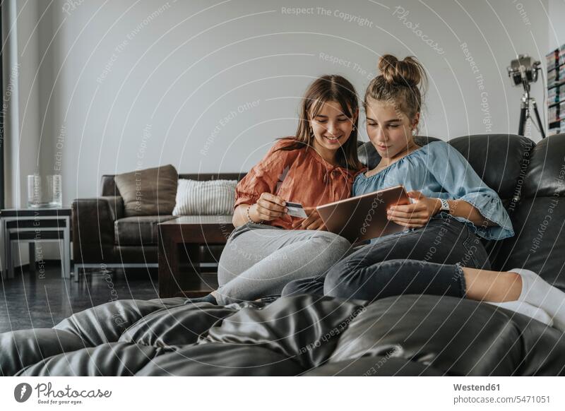 Friends doing online shopping over digital tablet while relaxing on sofa at home color image colour image Germany indoors indoor shot indoor shots interior