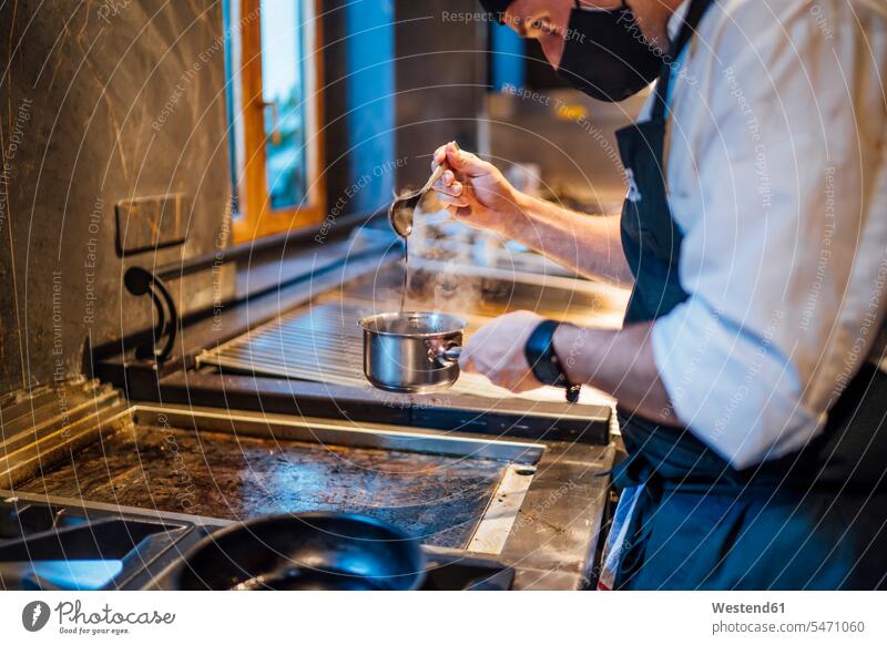 Chef wearing protective face mask preparing a sauce in restaurant kitchen human human being human beings humans person persons caucasian appearance