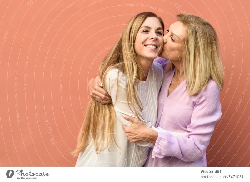 Happy mature woman hugging and kissing her daughter at a red wall friends mate female friend difference in age kisses smile embrace Embracement delight
