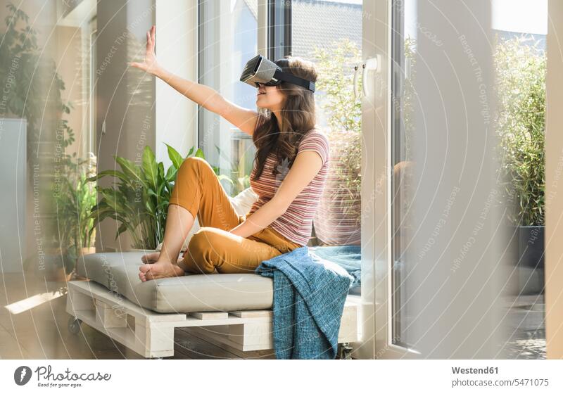 Young woman sitting at the window at home wearing VR glasses windows virtual females women Seated specs Eye Glasses spectacles Eyeglasses Adults grown-ups