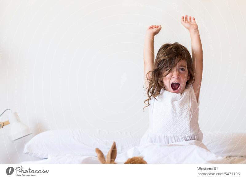 Little girl sitting on bed stretching beds Seated females girls child children kid kids people persons human being humans human beings raising arms arm up