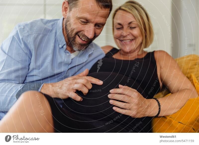Mature man and his pregnant mature wife sitting on couch touching her belly Seated bellies abdomen human abdomen Pregnant Woman upper body