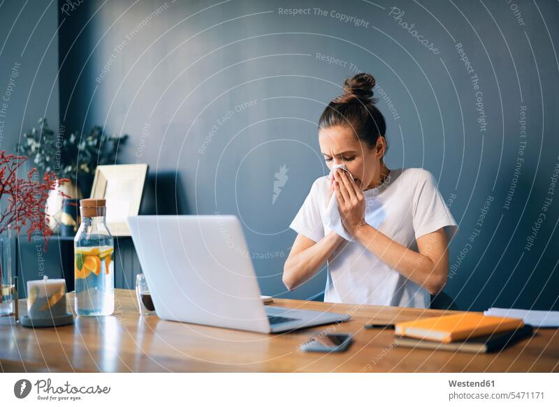 Businesswoman blowing nose while sitting at desk in home office color image colour image casual clothing casual wear leisure wear casual clothes Casual Attire