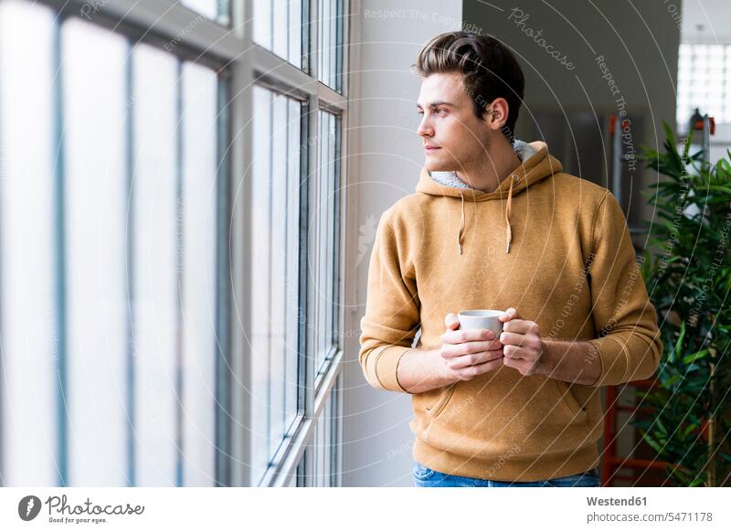 Young man with coffee cup contemplating while looking through window in new apartment color image colour image indoors indoor shot indoor shots interior