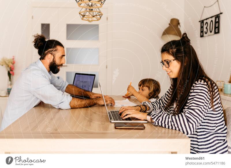 Woman working over laptop while father and daughter painting on dining table at home color image colour image indoors indoor shot indoor shots interior