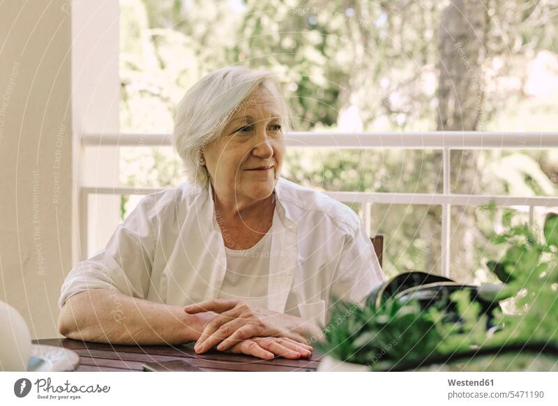 Thoughtful senior woman looking away while sitting at table in balcony color image colour image Spain leisure activity leisure activities free time leisure time