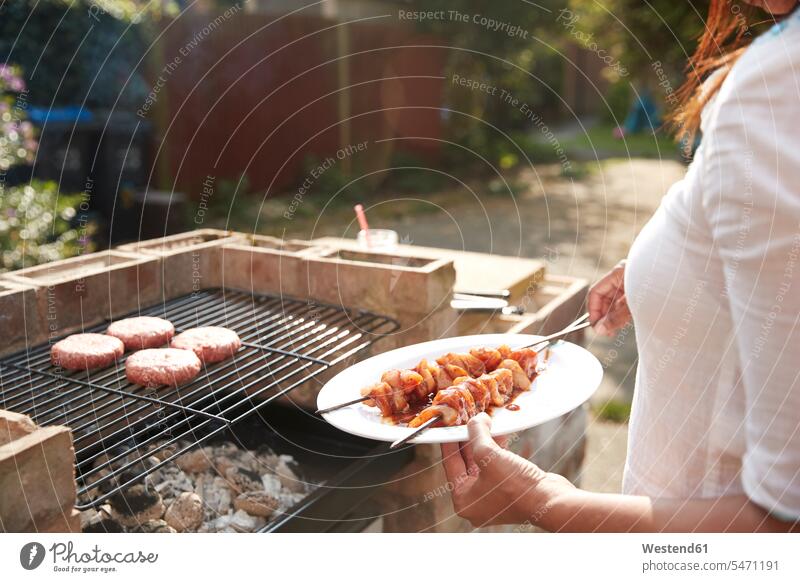 Midsection of woman holding plate with skewers while standing by barbecue grill at back yard on sunny day color image colour image outdoors location shots