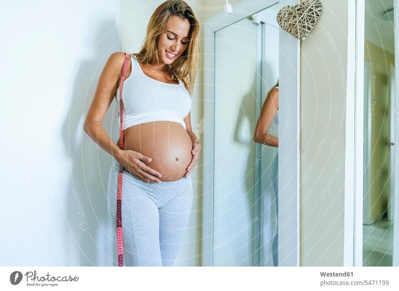 Pregnant woman looking at her belly in front of the mirror eyeing females women pregnant Pregnant Woman bellies stomach stomachs mirrors view seeing viewing