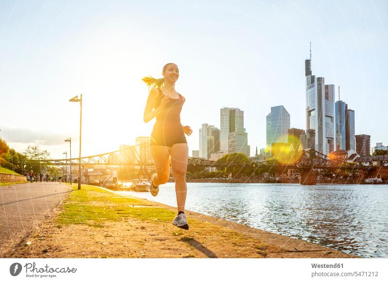 Germany, Hesse, Frankfurt, Young woman jogging along bank of Main river at sunset outdoors location shots outdoor shot outdoor shots sunsets sundown atmosphere