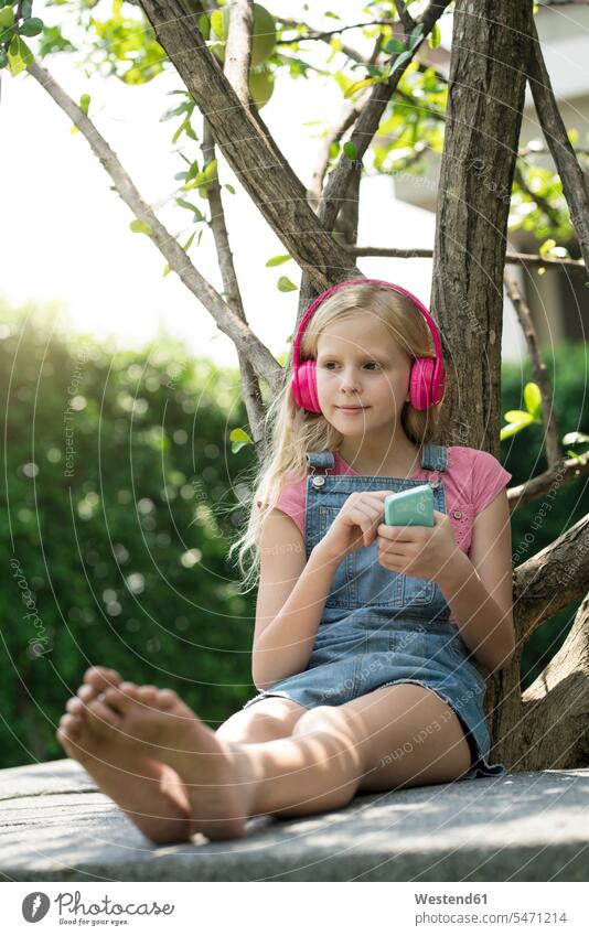 Cute blonde girl listening to music with pink headphones in garden headset magenta cute twee Cutie females girls gardens domestic garden hearing colour colours