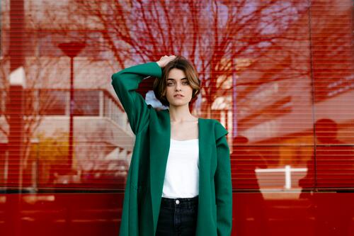 Young woman wearing green coat in front of a glass pane windows glass panes content Contented Emotion pleased Distinct individual Lifestyle fashionable