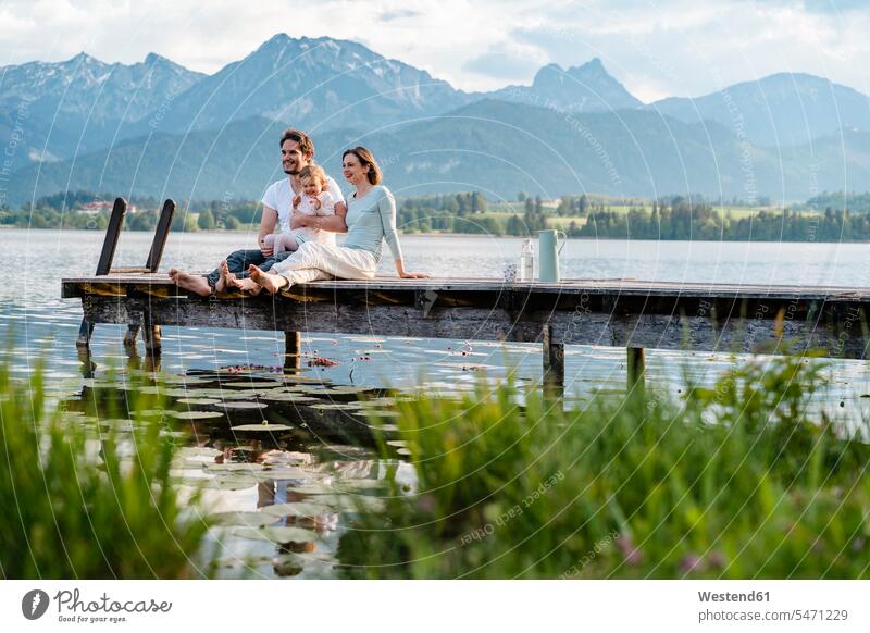 Happy family looking at view while sitting on jetty over lake against mountains color image colour image Germany leisure activity leisure activities free time