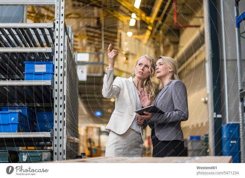 Two women with tablet talking in factory storehouse industrial hall shop floor factory hall industrial buildings speaking factories storage warehouse woman