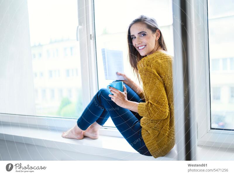 Young woman sitting on windowsill with book and cup of tea looking at camera human human being human beings humans person persons celibate celibates singles