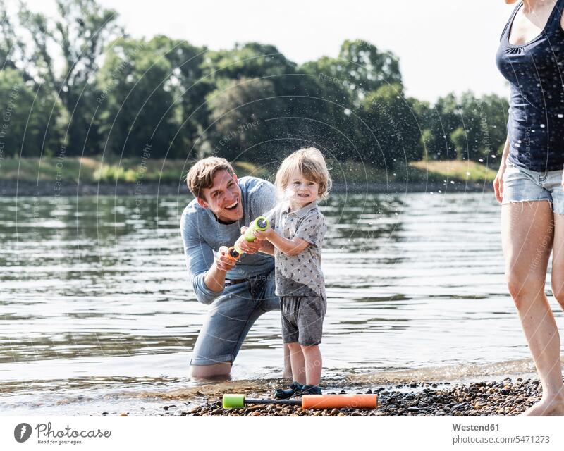 Father and son having fun at the riverside, playing with a water gun riverbank Water gun Fun funny laughing Laughter father pa fathers daddy dads papa sons