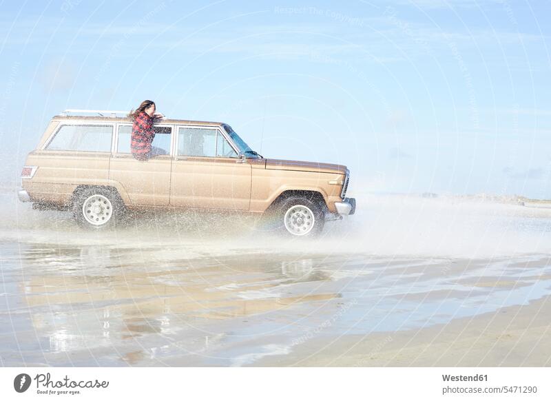Germany, St Peter-Ording, girl leaning out of window of off-road vehicle driving through water on the beach Fun having fun funny beaches females girls father pa