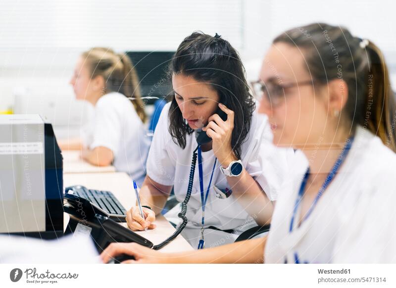 Female pharmacist writing while talking over telephone at desk in hospital color image colour image Spain indoors indoor shot indoor shots interior
