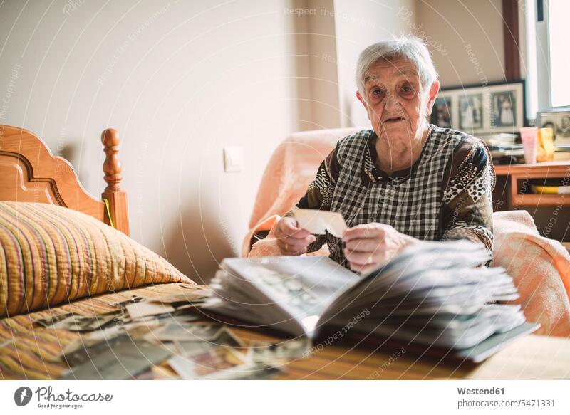 Portrait of senior woman adding old photos to a photo album at home photograph photographs senior women elder women elder woman photograph album photo albums