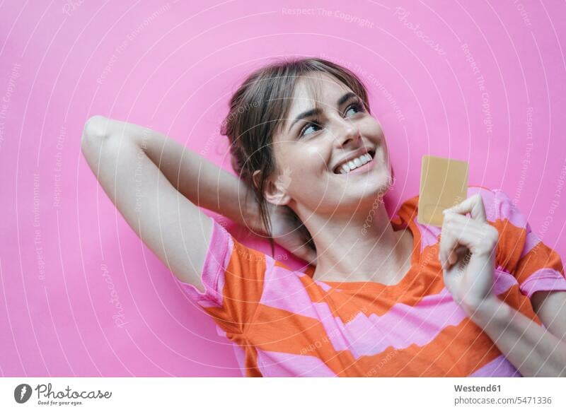 Woman lying on pink background with hands behind head, holding credit card debit card Pink background magenta hands behind neck Hand Behind Head woman females