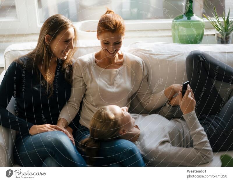 Happy mother with two teenage girls on couch at home with cell phone Teenage Girls female teenagers settee sofa sofas couches settees mobile phone mobiles