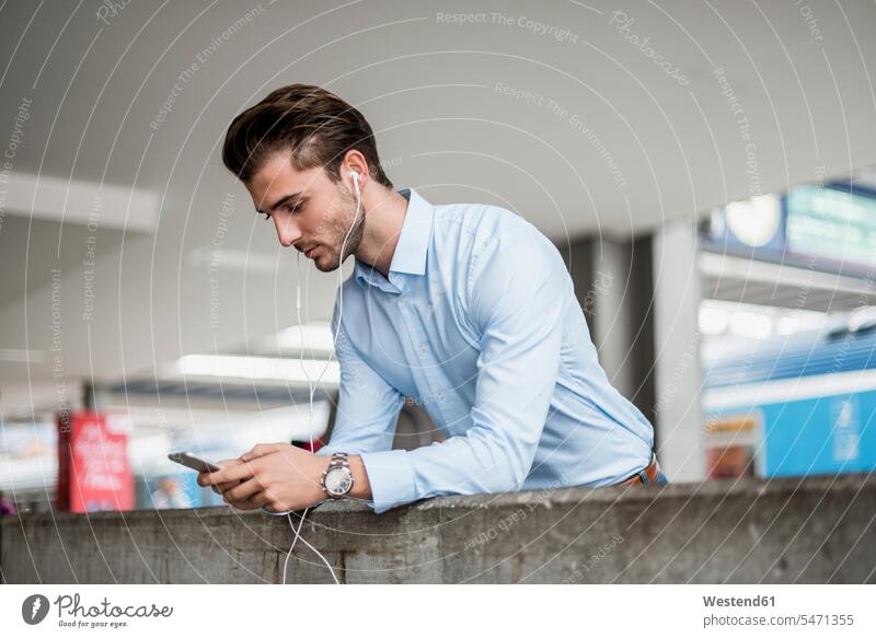 Businessman with cell phone and earbuds at the station Business man Businessmen Business men earphones ear phone ear phones mobile phone mobiles mobile phones