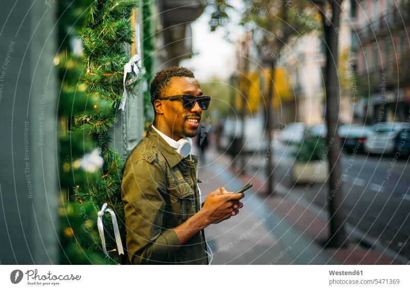 Young man wearing sunglasses using smart phone while standing on sidewalk in city color image colour image Spain leisure activity leisure activities free time