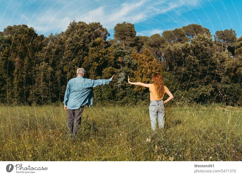 Rear view of woman and senior man with masks standing on meadow, safety distance reclusive reclusively risky protect protecting Safety secure on the go