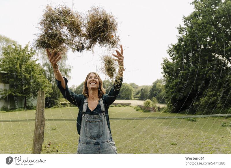 Happy young woman in the countryside throwing up hay smile delight enjoyment Pleasant pleasure Cheerfulness exhilaration gaiety gay glad Joyous merry happy