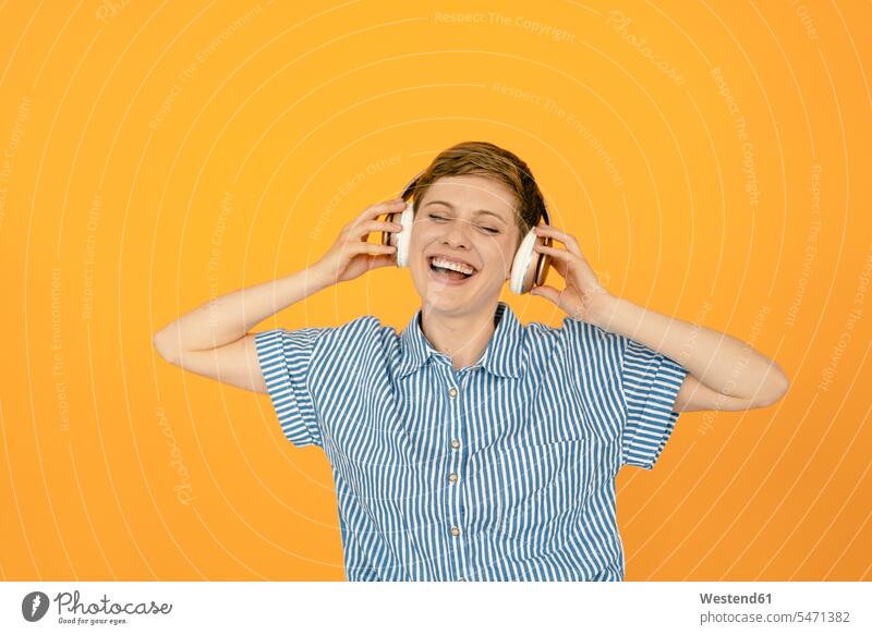 Portrait of happy woman listening to music with orange background human human being human beings humans person persons short hairs short hairstyle