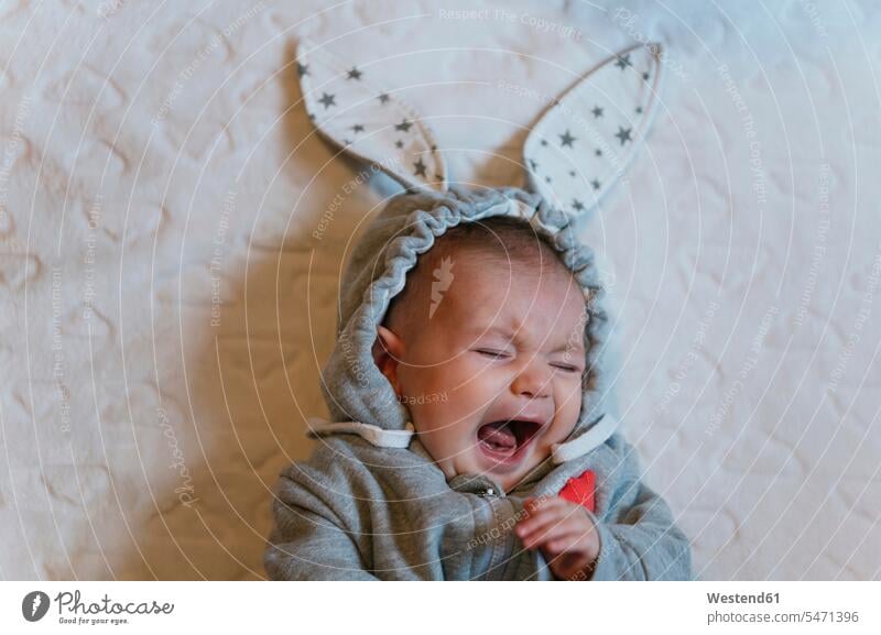 Portrait of crying baby girl in a rabbit hoodie lying on white blanket Blankets hoods Bed - Furniture beds scream shout shouting Emotions Feeling Feelings
