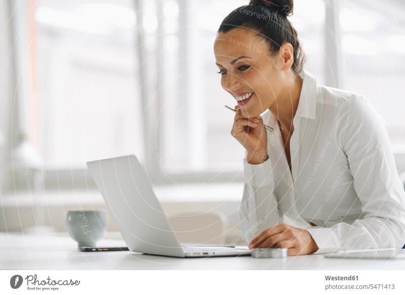 Smiling businesswoman using laptop on desk in home office color image colour image Germany indoors indoor shot indoor shots interior interior view Interiors