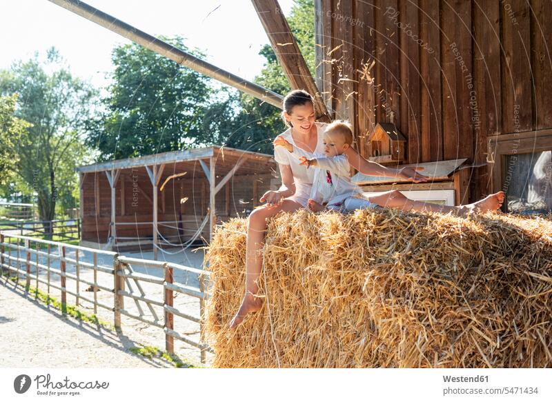 Happy mother and little daughter playing with straw in a barn Straw happiness happy mommy mothers ma mummy mama daughters farm agriculture parents family