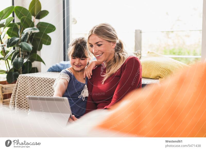 Happy mother and daughter using tablet at home windows video smile Seated sit relax relaxing relaxation delight enjoyment Pleasant pleasure Cheerfulness
