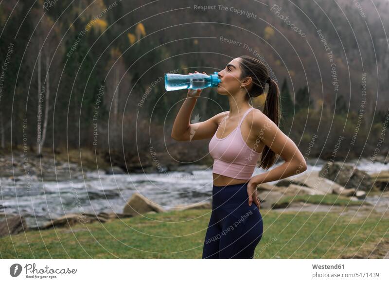 Exhausted young woman drinking water while standing with hand on hip, Ordesa National Park, Huesca, Spain color image colour image outdoors location shots