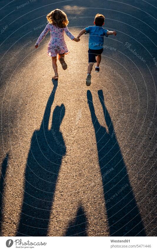 Rear view of siblings holding hands and running on road color image colour image Canada leisure activity leisure activities free time leisure time