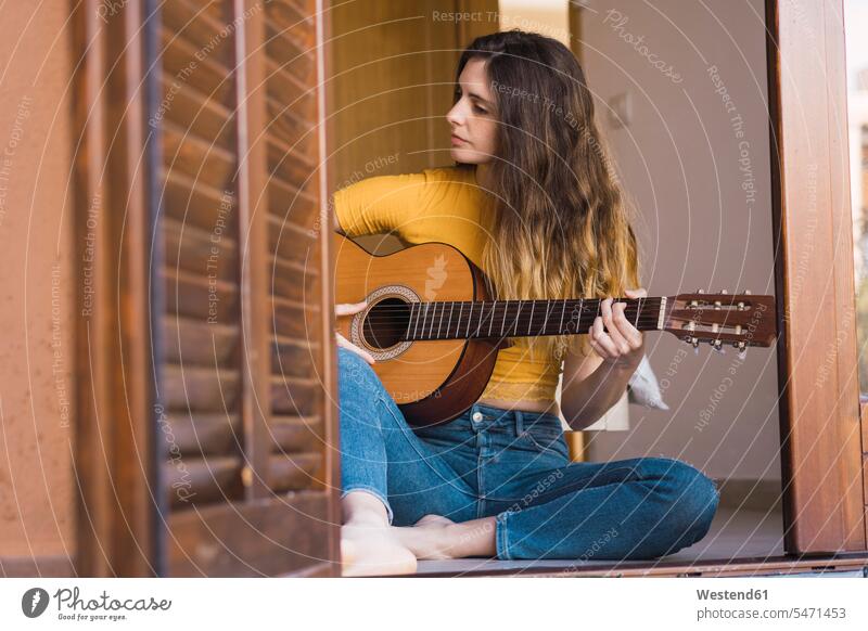 Young woman sitting on the floor at home playing guitar Seated guitars females women Floor Floors stringed instrument stringed instruments musical instrument