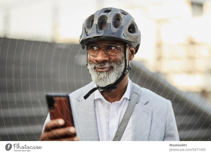 Portrait of smiling mature businessman with smartphone wearing cycling helmet and glasses business life business world business person businesspeople