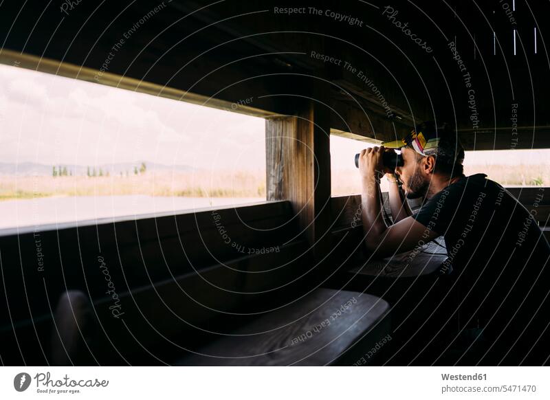 Man birdwatching with binoculars from a viewing tower raised hide deer stand high seat man men males observing observe Exploration exploring explore