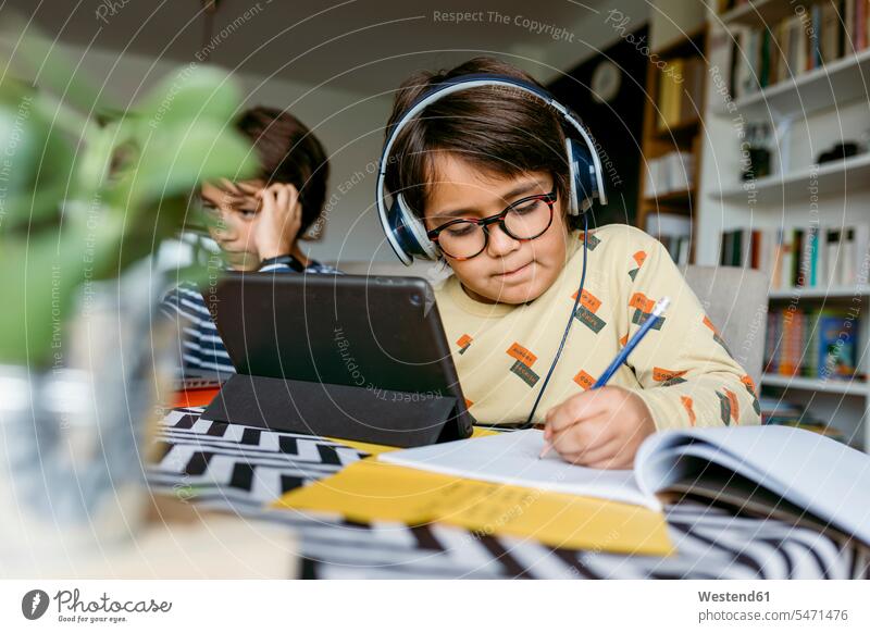 Boy writing notes through digital tablet sitting with male friend during e-Learning at home color image colour image 8-9 years 8 to 9 years children kid kids