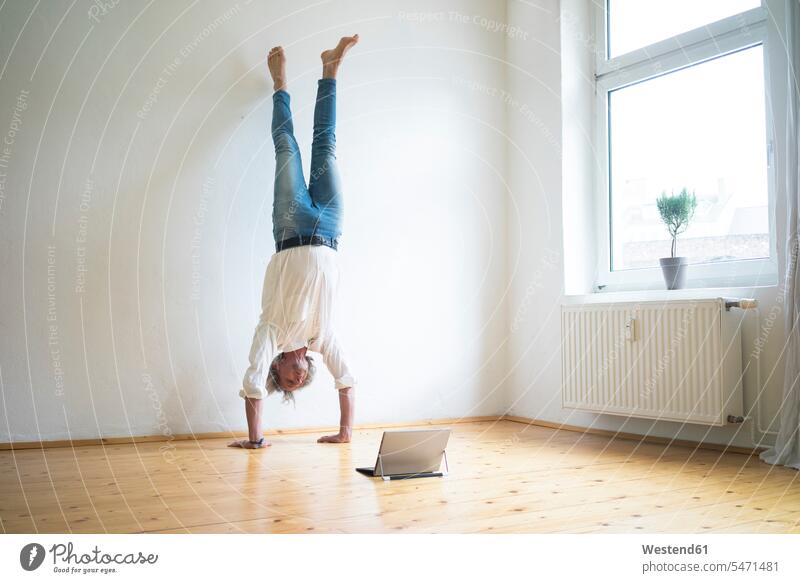 Mature man doing a handstand on floor in empty room looking at tablet rooms domestic room domestic rooms men males emptiness floors digitizer Tablet Computer