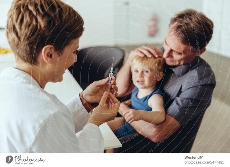 Father holding son while being vaccinated by pedeatrician sons manchild manchildren baby boys male father pa fathers daddy dads papa pediatrician