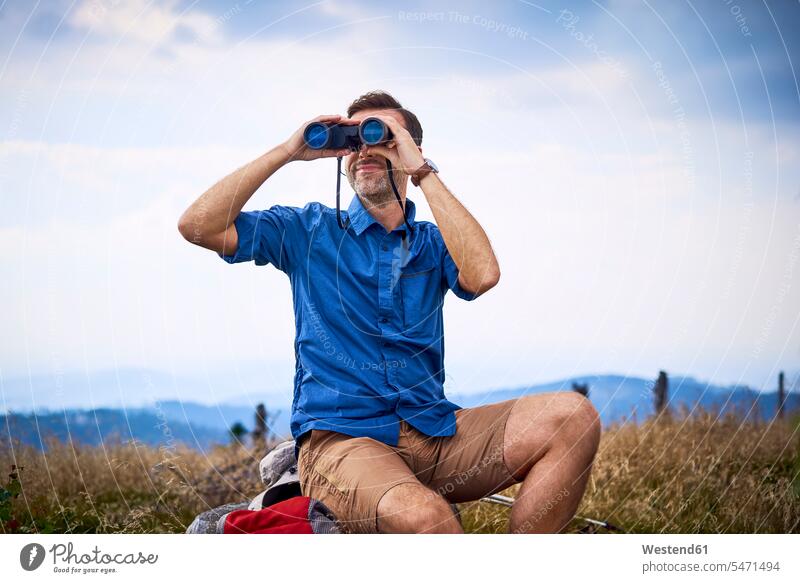 Man looking through binoculars during hiking trip man men males view seeing viewing hike Adults grown-ups grownups adult people persons human being humans
